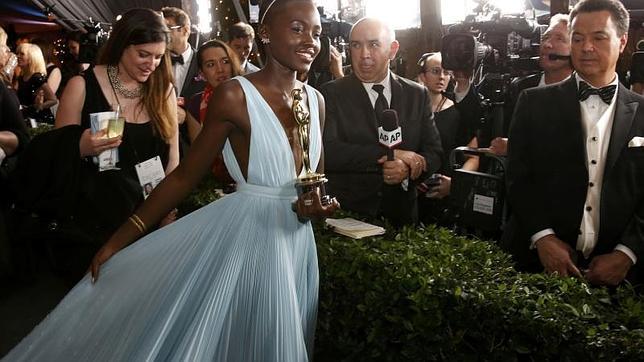 Lupita Nyong'o a la salida de los premios del cine, estatuilla en una mano y la cola de su vestido en otra