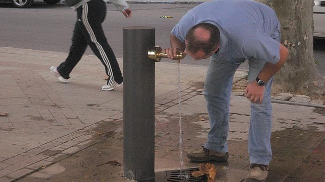 Un hombre bebe agua en una fuente pública