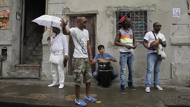 Un joven  espera el transporte público junto a unos músicos en una calle de La Habana
