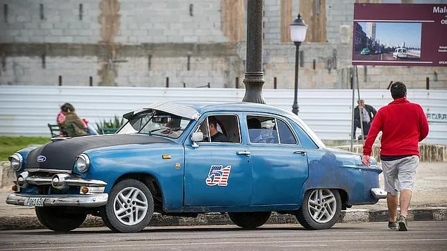 Un vehículo antiguo, con una bandera de EE.UU. en la puerta, pasa por una calle de La Habana
