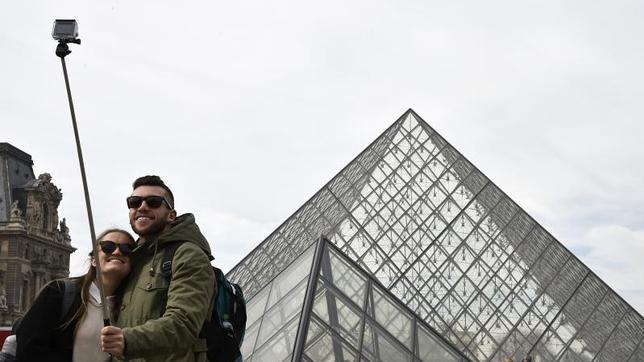Dos turistas utilizan un paloselfi junto al Louvre, en París