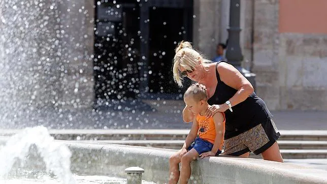 Una madre refresca a su hijo en una fuente