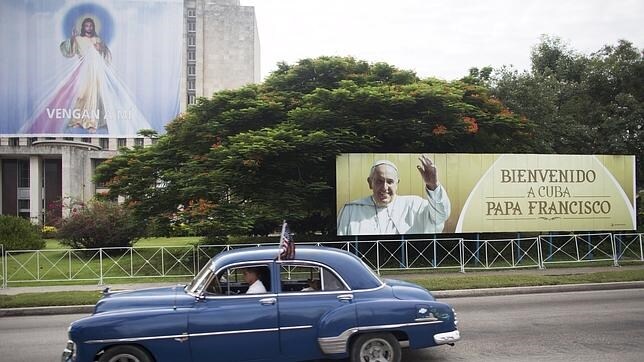 Un vehículo antiguo pasa junto a un anuncio del viaje del Papa Francisco y una imagen de Jesús, en La Habana
