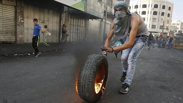 Un joven palestino se prepara para lanzar un neumático en llamas contra las fuerzas israelíes en Hebrón