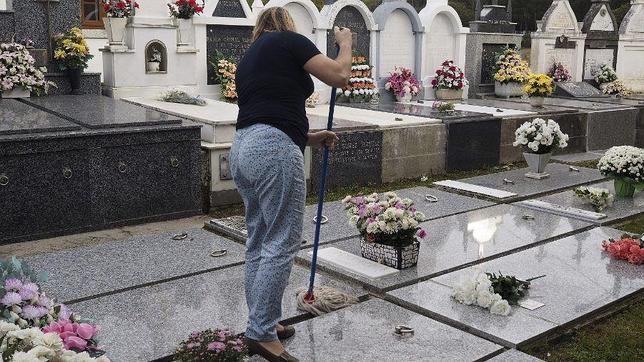 Una mujer limpia las placas de las tumbas de un cementerio