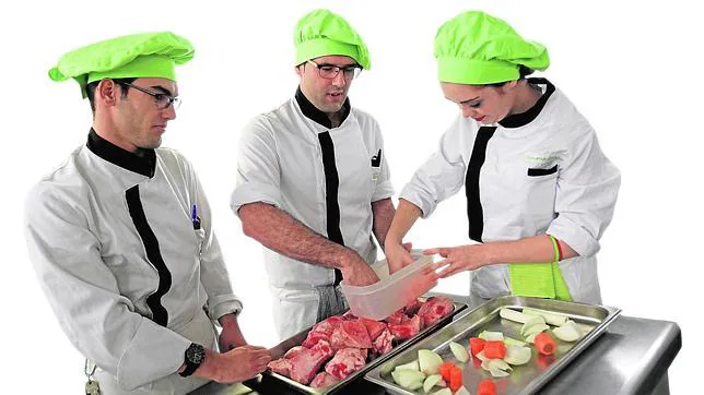 Tres alumnos de Cocina, en clase, ataviados con uniformes y gorros de chef