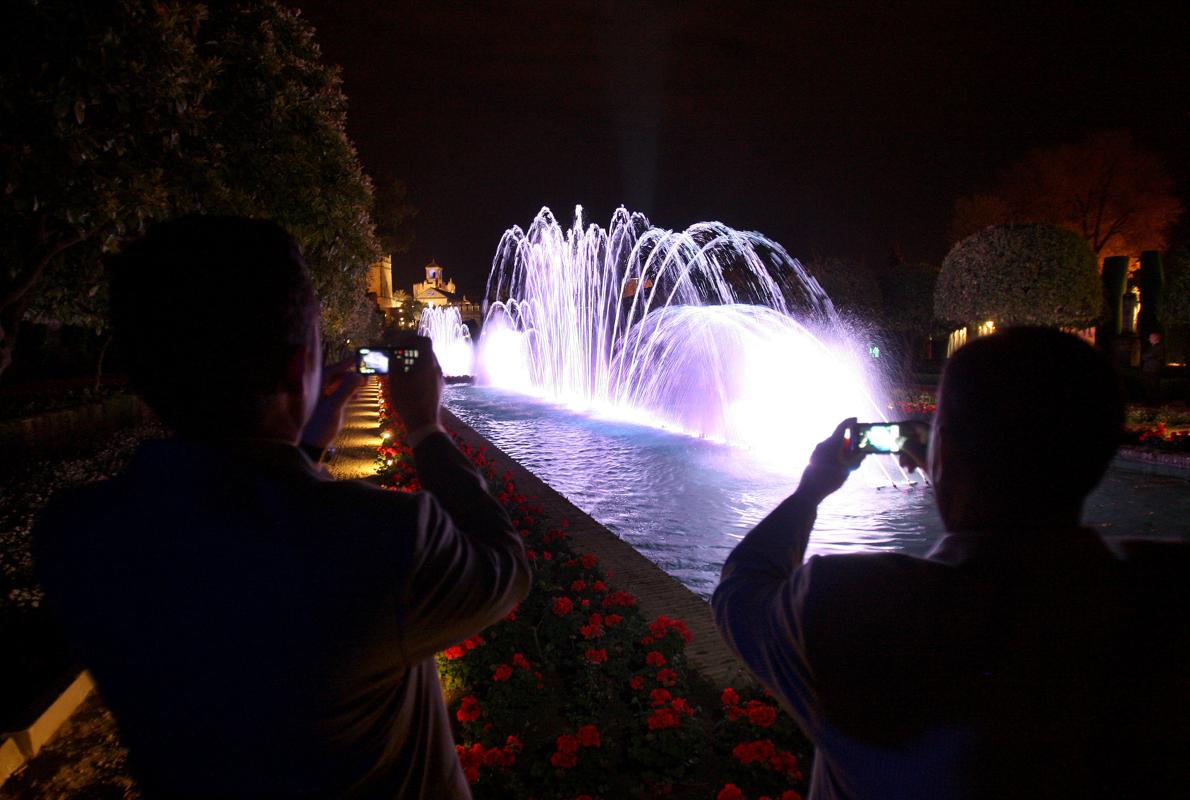 Dos turistas toman fotos con sus móviles del espectaculo de luces y sonido del Alcázar