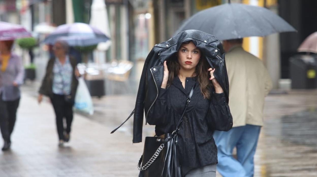 Una joven se protege la cabeza con una cazadora, en la calle Cruz Conde