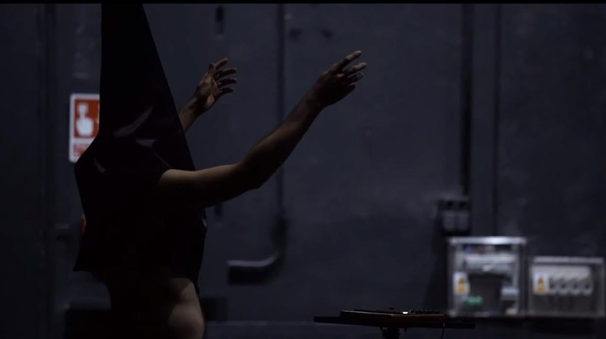 Una escena de «Dios tiene vagina», con un hombre desnudo vestido de nazareno