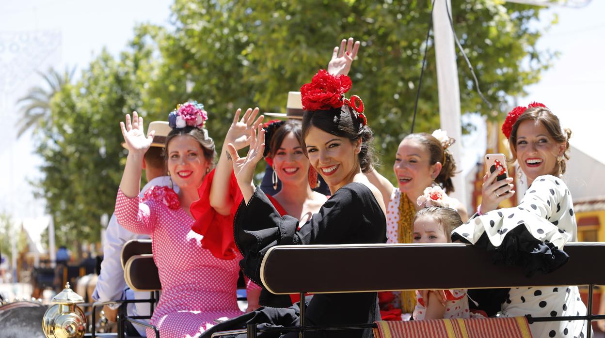 Un grupo de mujeres saluda desde un coche de caballos en la Feria de Córdoba