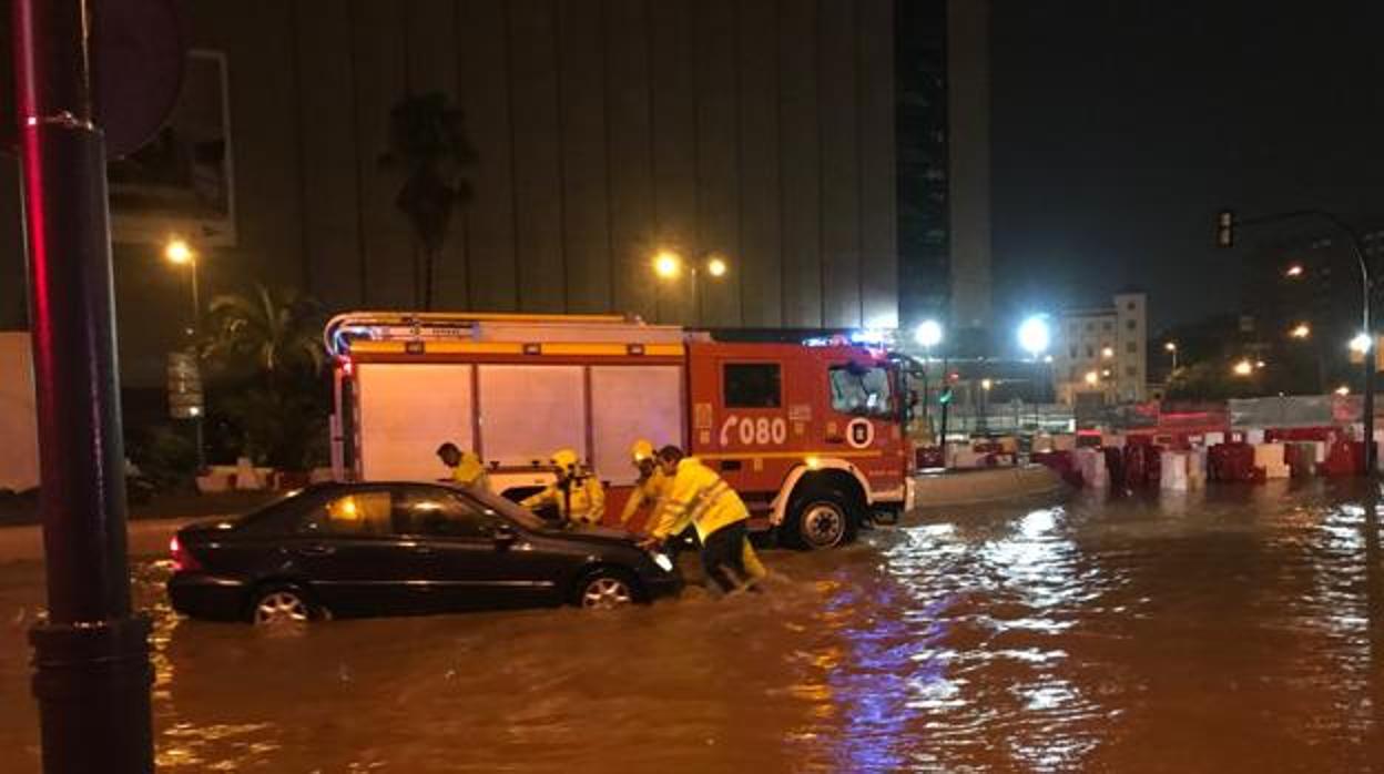Bomberos ayudan a un vehículo a salir del agua junto a la explanada del El Cortel Inglés
