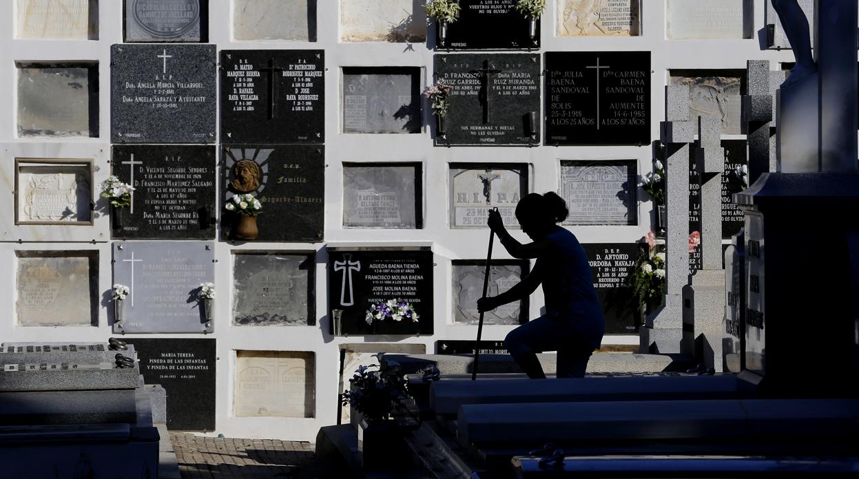 Una mujer limpia la lápida de una tumba en el cementerio de la Salud