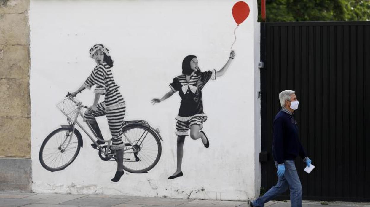 Un hombre pasa delante de un graffiti urbano en el centro de Córdoba en la jornada del Martes Santo