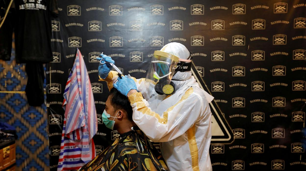 Un barbero protegido por un traje contra el coronavirus pela a un hombre en Indonesia