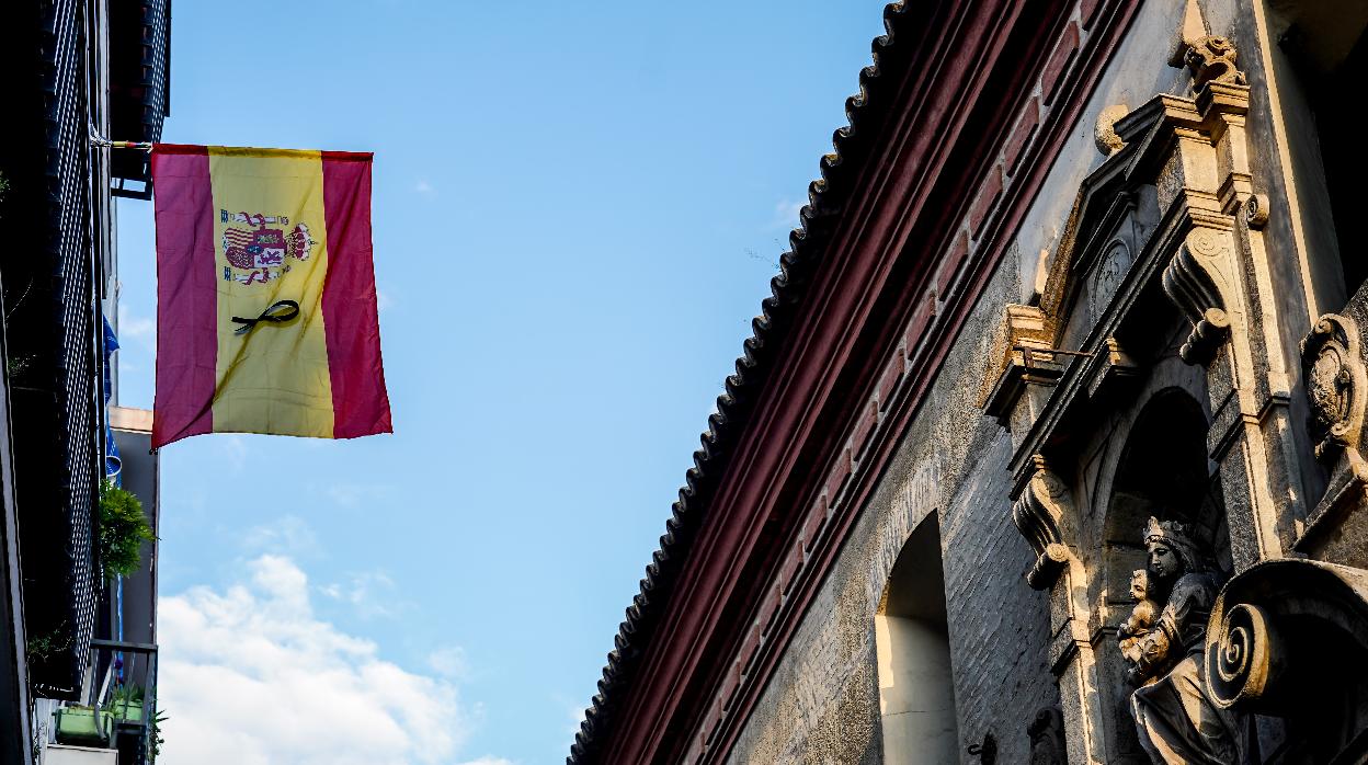 Una bandera de España con crespón negro en señal de duelo por las víctimas del coronavirus en un balcón sevillano