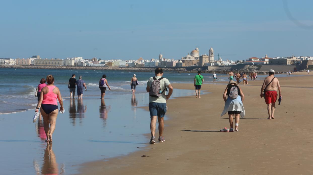 Vecinos de Cádiz pasean por la playa con la catedral al fondo