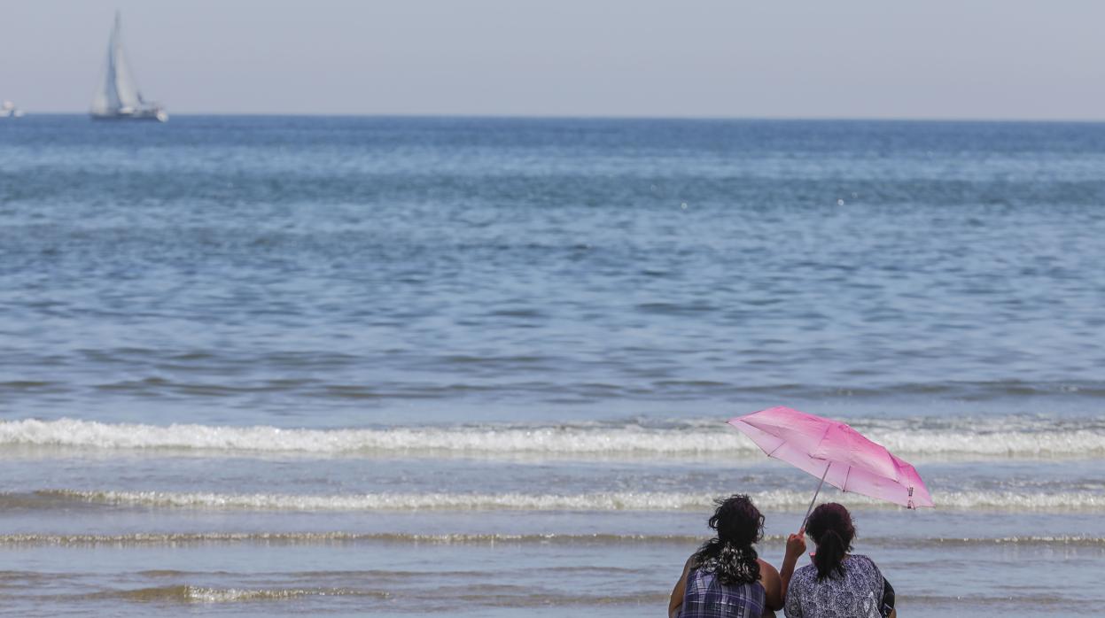 Dos mujeres observan un velero desde la playa