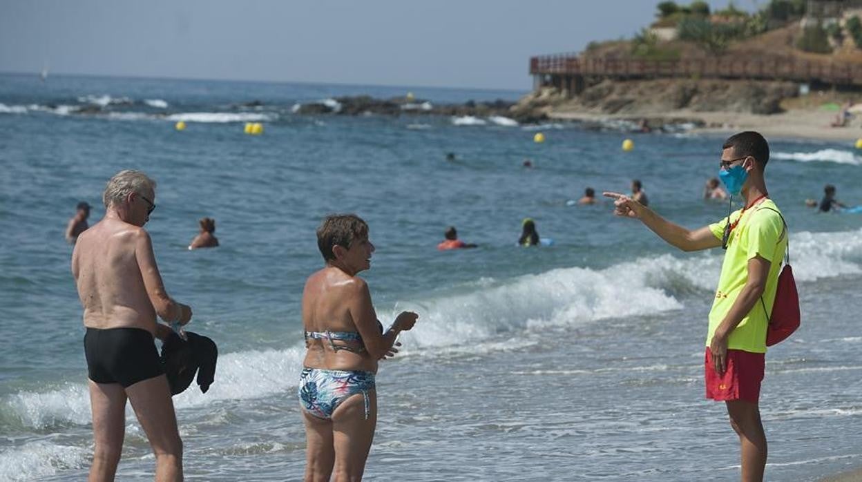 Un socorrista le indica a dos personas que deben ponerse la mascarilla en una playa de Málaga