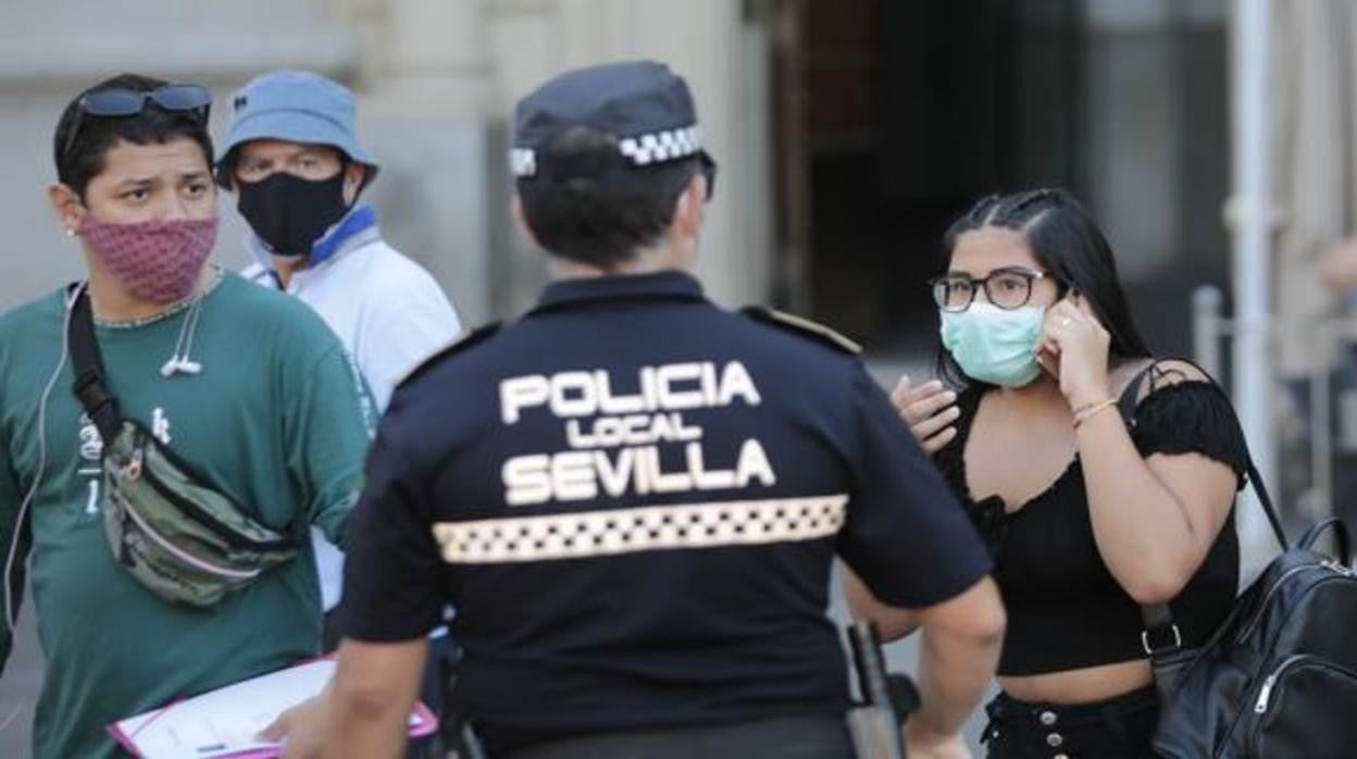 Tres ciudadanos con mascarilla y un agente de la Policía Local de Sevilla