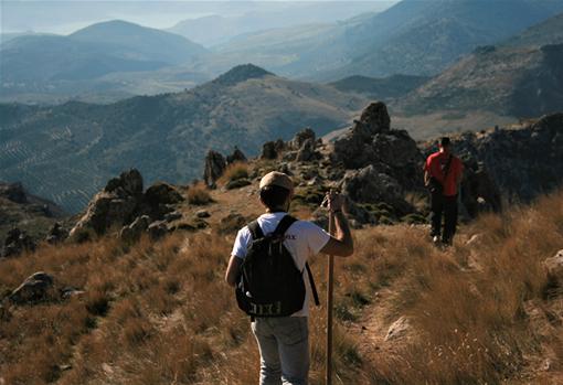 Dos senderistas caminan por otro de los senderos de subida con las Sierras Subbéticas al fondo
