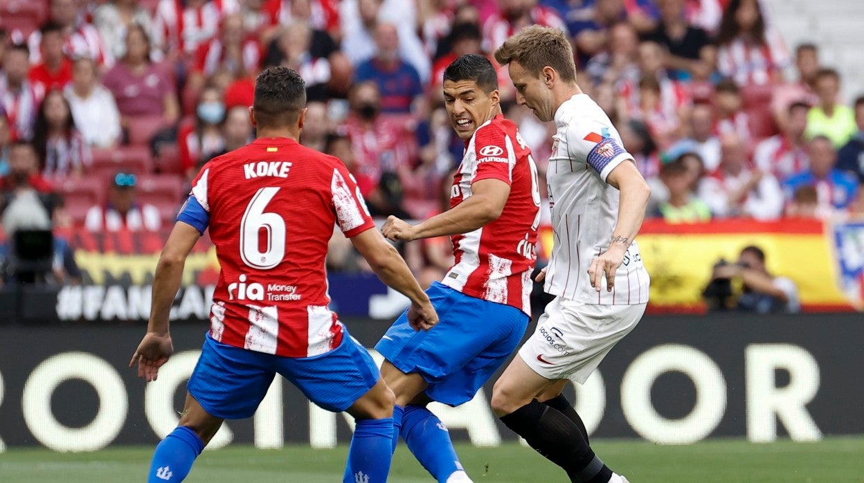 Ivan Rakitic trata de hacerse con el balón entre Koke y Luis Suárez