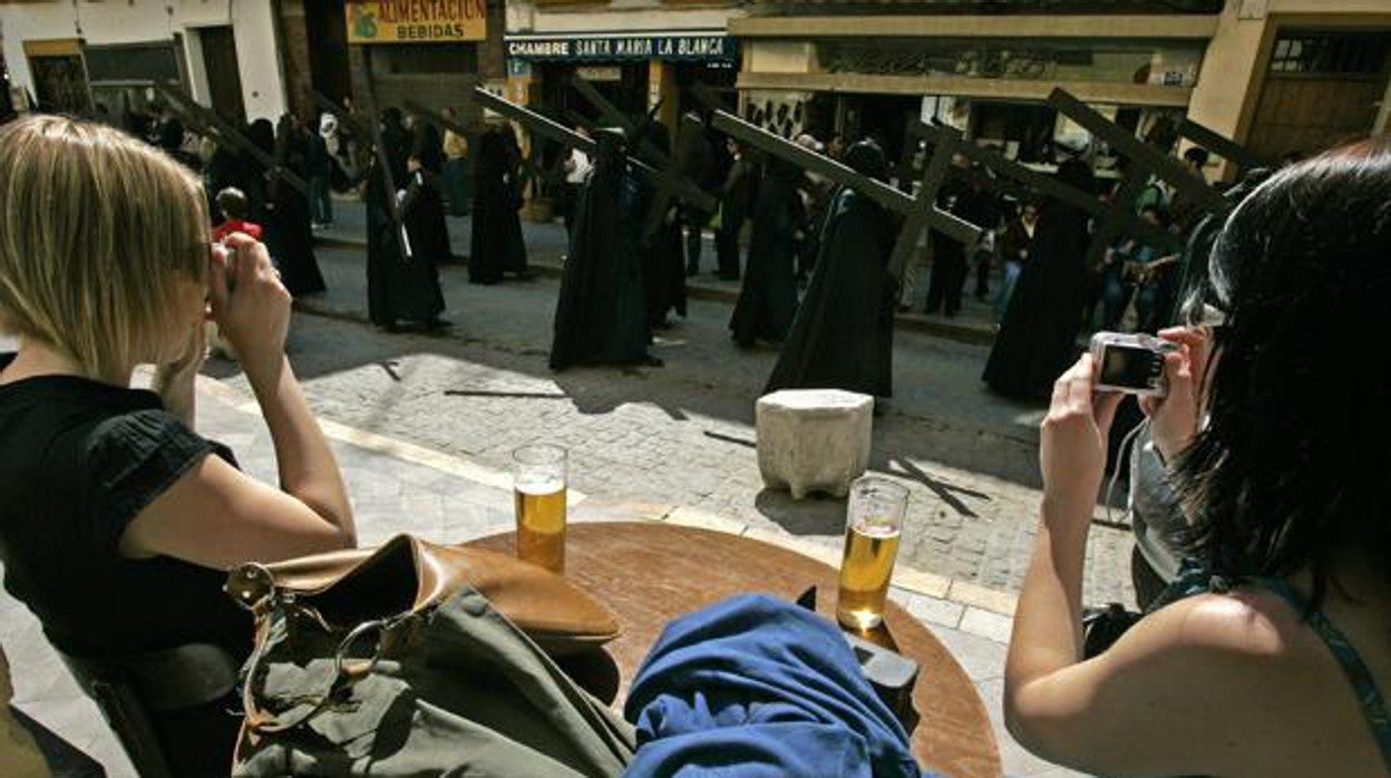 Comensales tomando una cerveza al paso de una cofradía en Sevilla