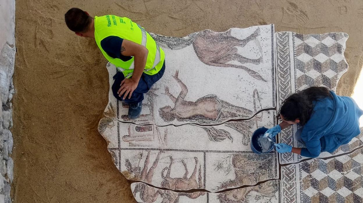 Dos personas trabajan sobre la restauración del mosaico «Los amores de Zeus»