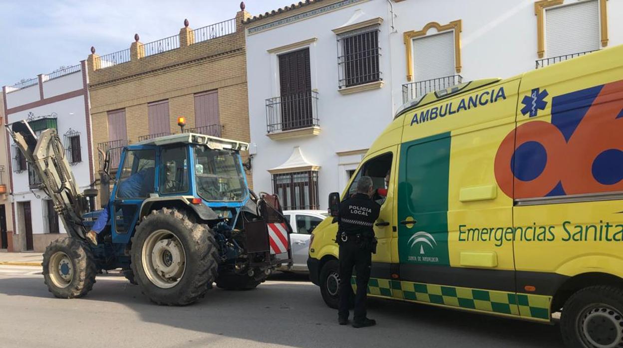 Un agente de la Policía Local de Arahal junto a una ambulancia y el tractor implicado