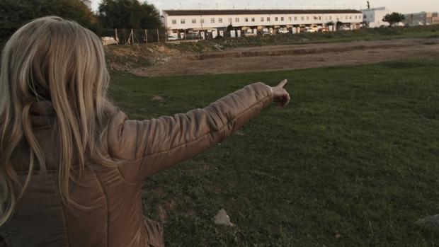 Una mujer señala la parcela afectada, cerca de unas viviendas