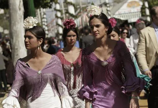 Unas jóvenes vestidas con el traje de flamenca pasean por la Feria