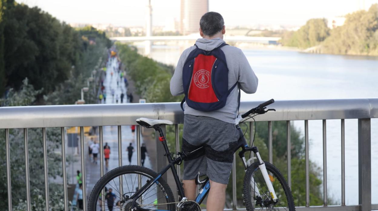 Un ciclista observa la riada de corredores por el paseo del río Guadalquivir