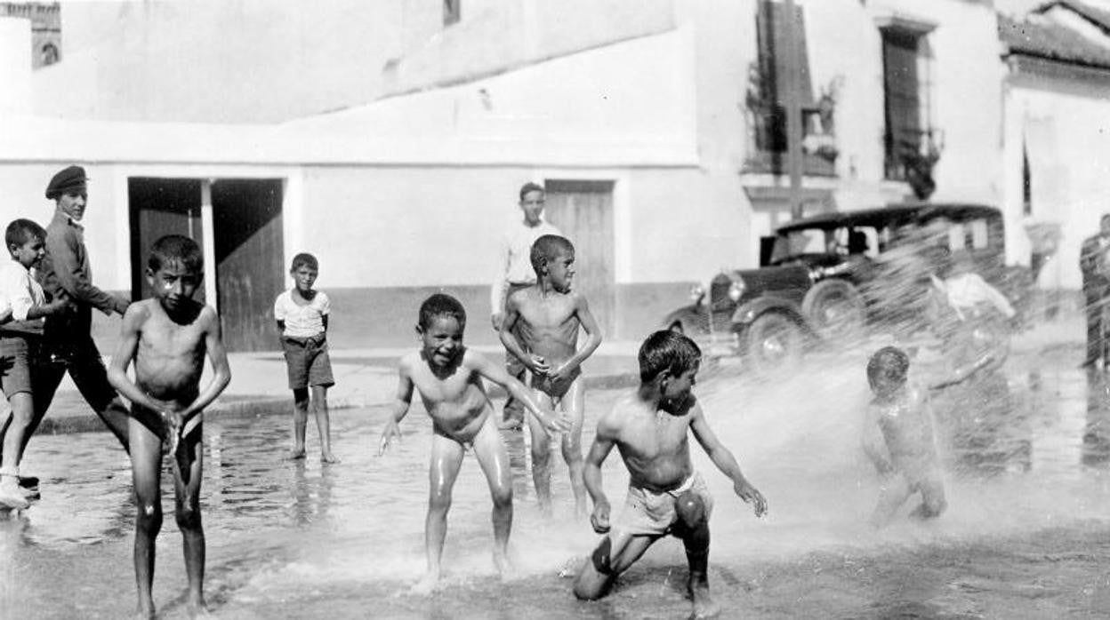 Un grupo de niños juega y se baña en plena calle con una manguera de riego en 1930