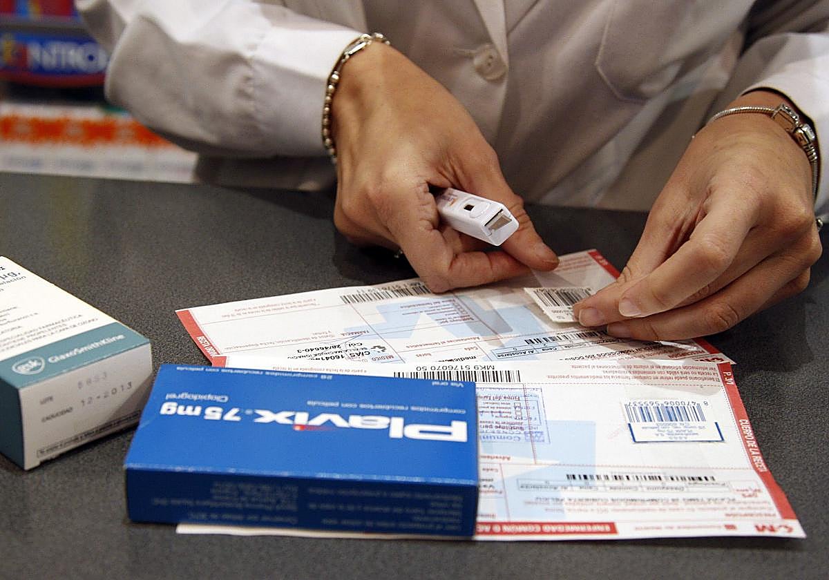 Una farmacéutica recorta el código de barras de varios medicamentos para posteriormente pegarlos a la receta expedida por el médico.