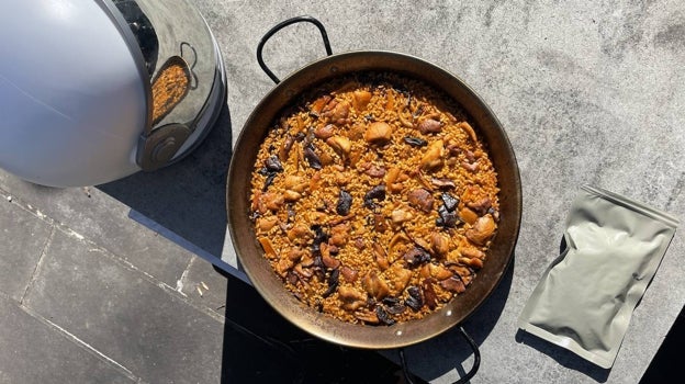 Una paella junto a un casco espacial y el sobre que contenía la paella elaborada por el chef José Andrés