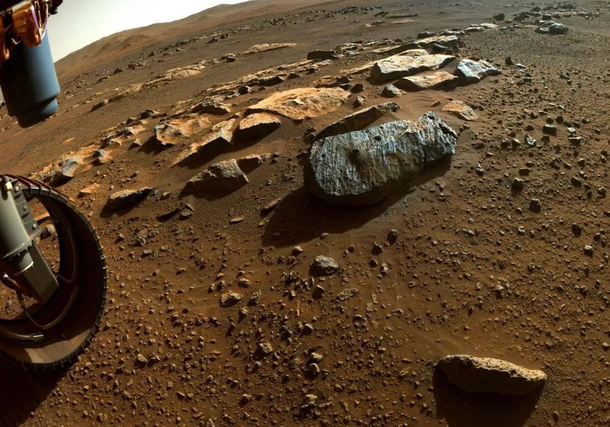 El rover Perseverance (a la izquierda) despuÃ©s de tomar muestras en una roca marciana (en el centro de la imagen). Se pueden observar los agujeros en la piedra