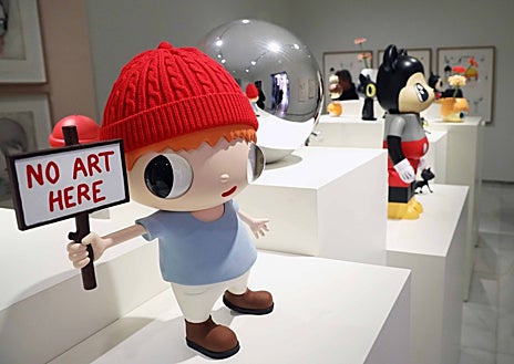 Imagen secundaria 1 - Sobre estas líneas, algunas de las colaboraciones y 'toys' del artista. A la derecha, su 'pequeño Maurizio'. Arriba, un fotógrafo se afana con una escultura monumental del gato Gunter