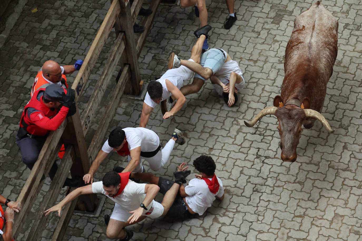 Varios participantes caen al suelo durante el quinto encierro de las fiestas de San Fermín