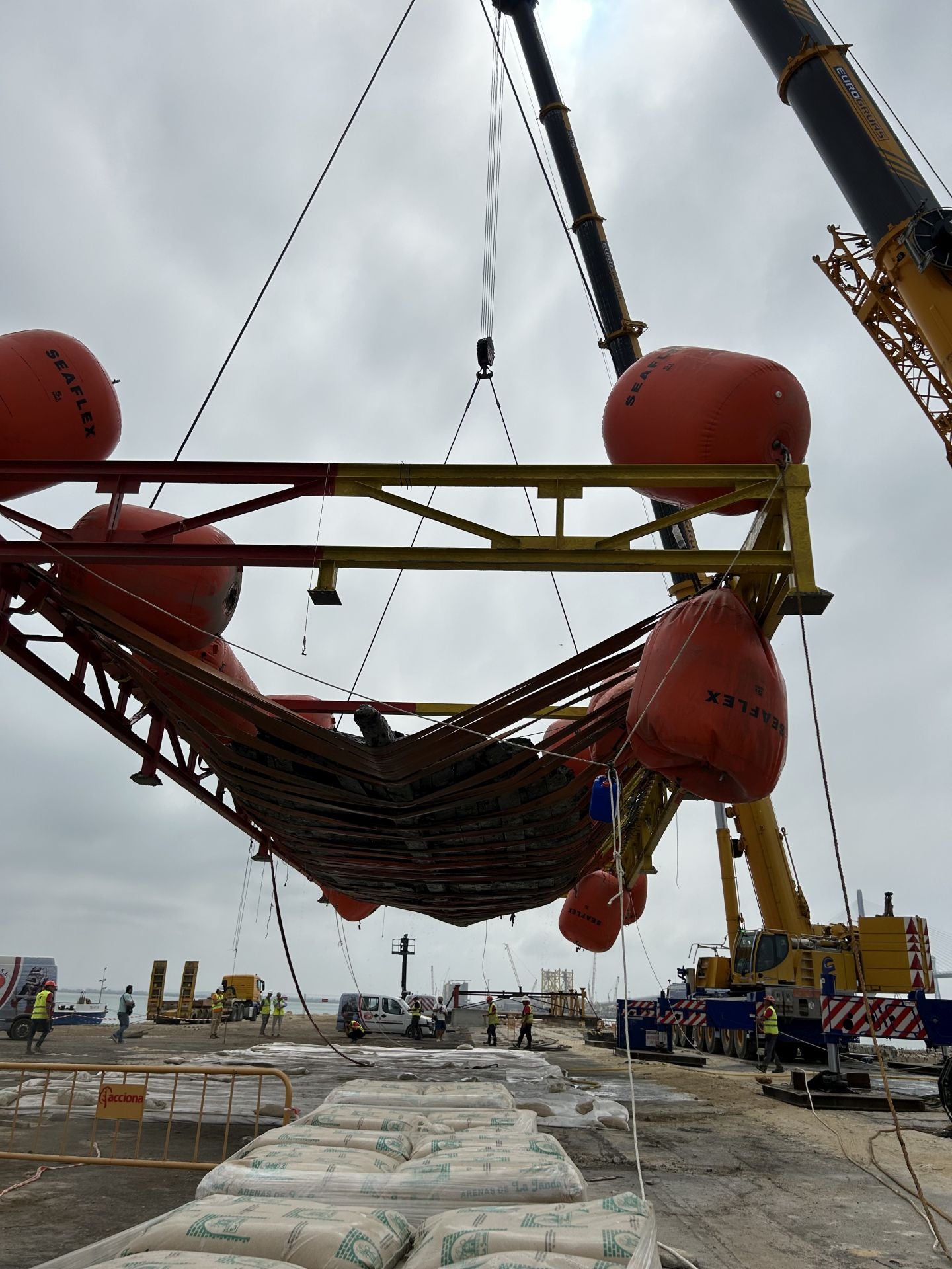 Una vez fuera del agua, las grúas han girado el pecio  para colocarlo sobre una cama de sacos terreros en el muelle