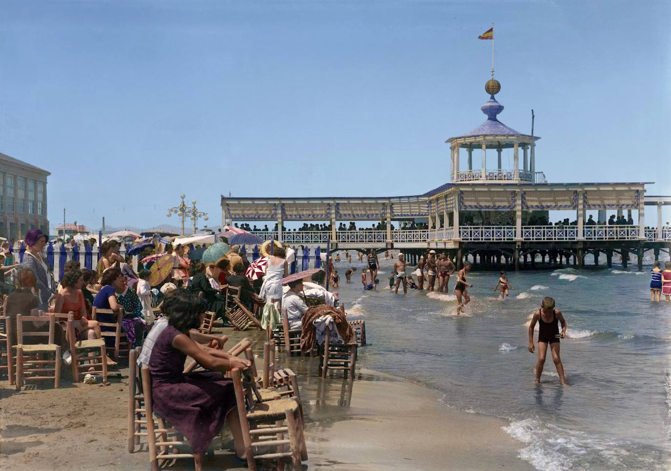 Pabellón del Balneario de las Arenas. (Década de 1920). En Valencia se disfrutaba del mar con otro estilo. Con sillas de enea. Y una característica especial: Una valla separaba, en la zona de arena de la playa, el espacio donde podían estar los hombres y las mujeres. Los matrimonios debían disfrutar del mar de un modo pintoresco, con los maridos separados de sus esposas por una valla. Original: Vicente Barberá Masip.