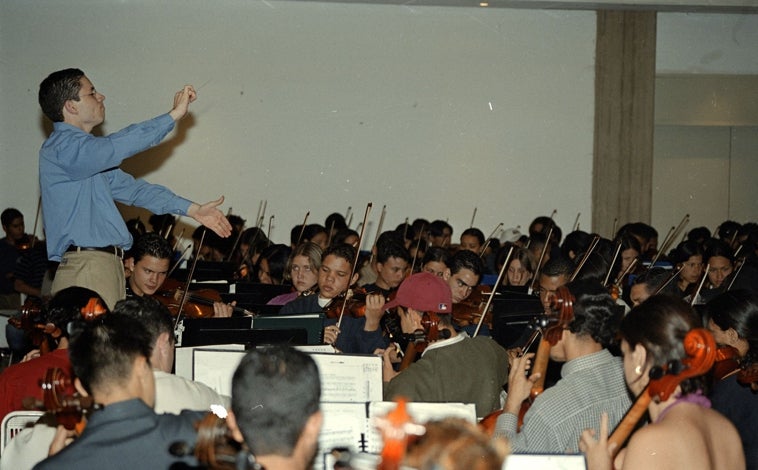 Imagen principal - Arriba, un joven Dudamel dirigiendo una orquesta de El Sistema (Foto: El Sistema). Derecha, Dudamel junto a El Sistema en la Philarmonie de Paris (Foto: Bertrand). Izquierda, Dudamel junto a la LA Phil en Coachella (Foto: Timothy Norris)