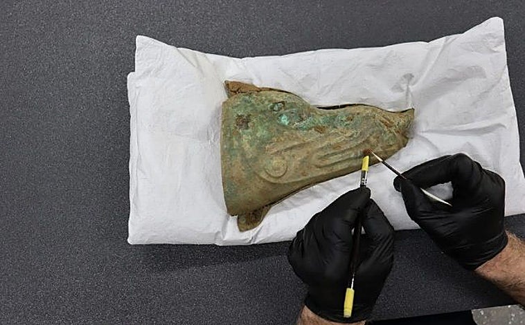 Imagen principal - El estandarte de jabalí, el conservador Jonathan Clark realizando la microexcavación y el carnyx recuperado