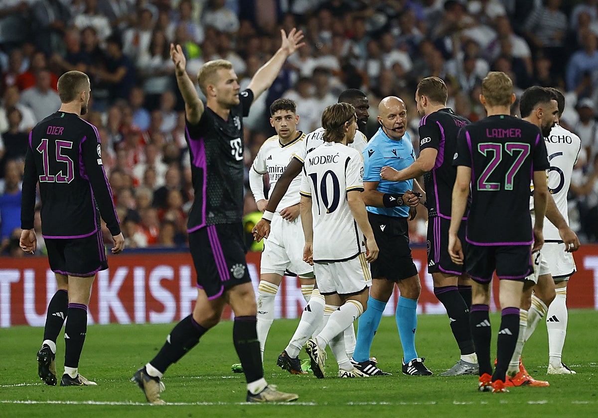 Los jugadores de ambos equipos rodean al árbitro del partido