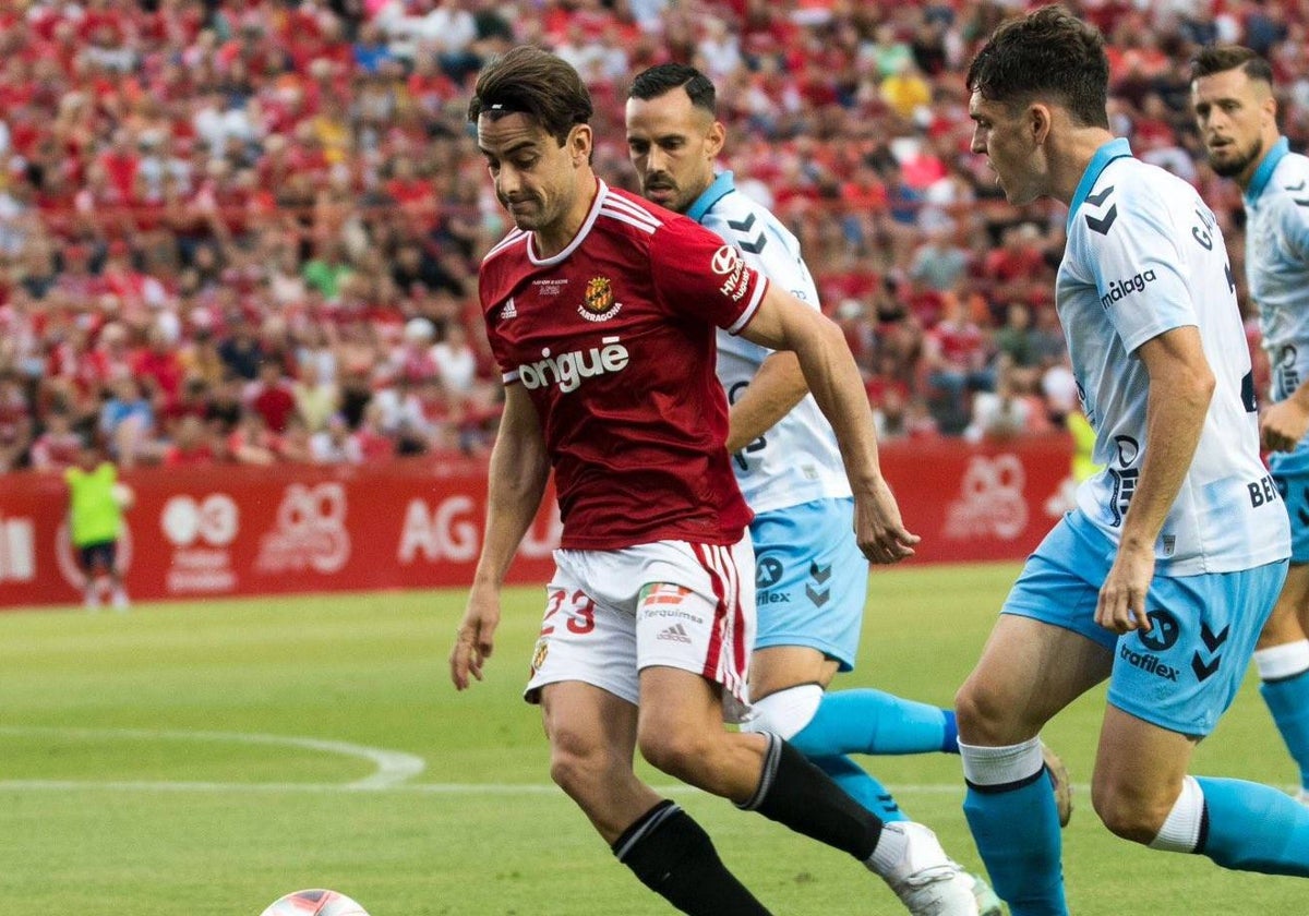 David Concha, jugador del Nástic, escoltado por la defensa malagueña en el partido que se jugó en el Nou Estadi Costa Daurada