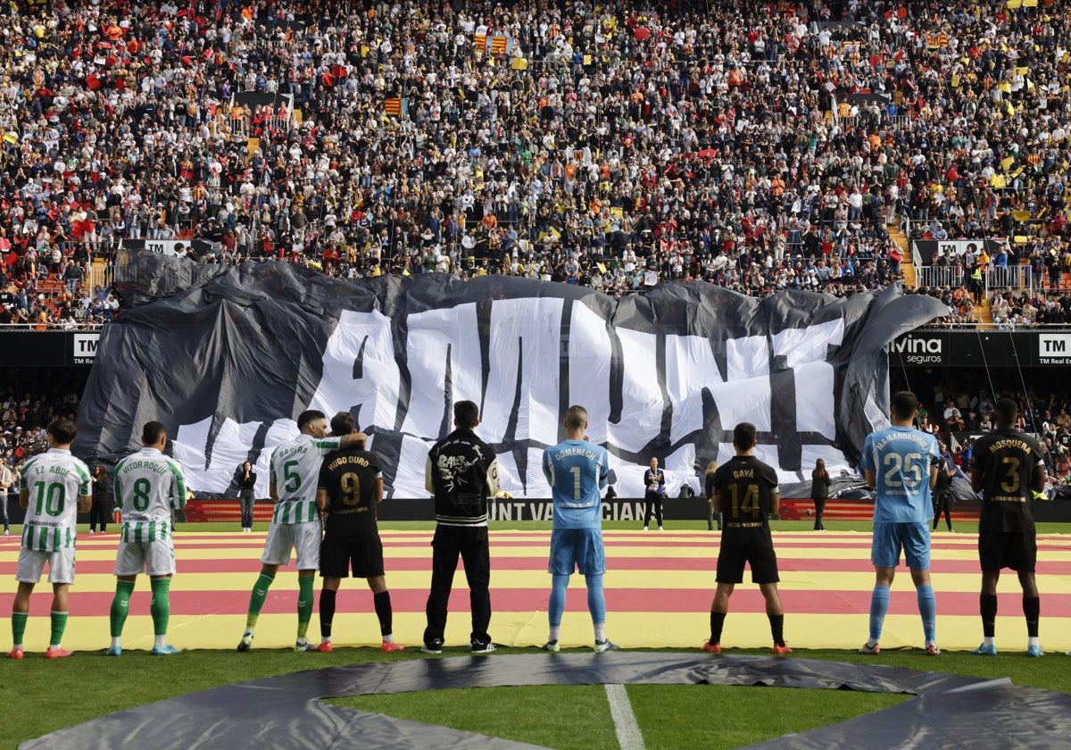 Jugadores del Valencia y Betis frente al tifo desplegado en Mestalla recordando a los municipios afectados por la DANA