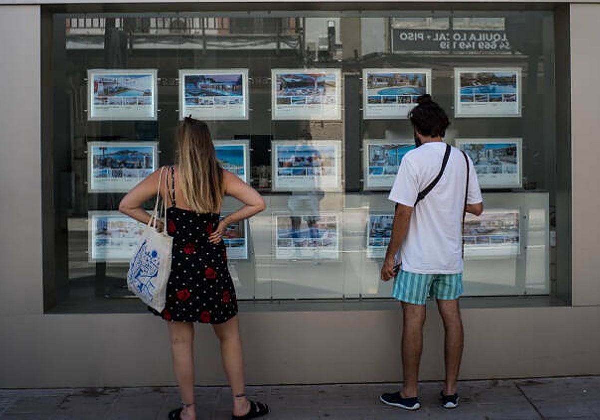 Dos jóvenes miran ofertas de vivienda frente a una inmobiliaria