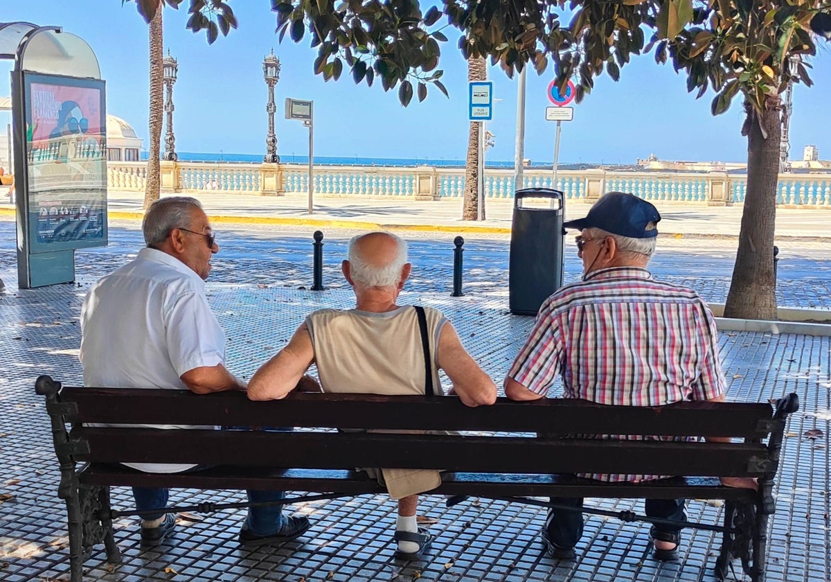 Tres personas en un banco frente a la playa de La Caleta (Cádiz)