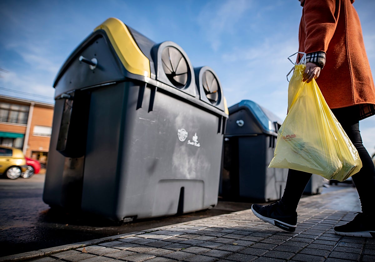Un mujer se dirige al contenedor amarillo a tirar botellas de plástico y otros envases