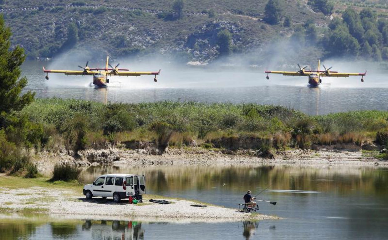 Un hombres pesca mientras dos hidroaviones recargan agua cerca del parque natural de la Sierra de Mariola