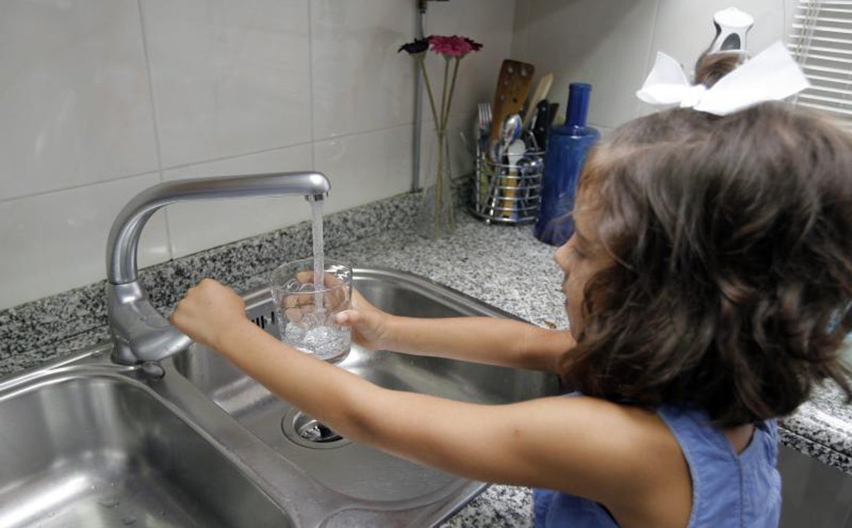 Una niña llena un vaso de agua en su casa