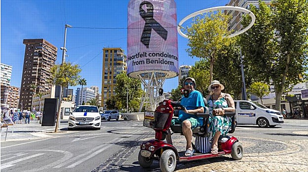 Dos turistas británicos pasan junto a la torre Tecnohito, con crespón negro en la imagen proyectada